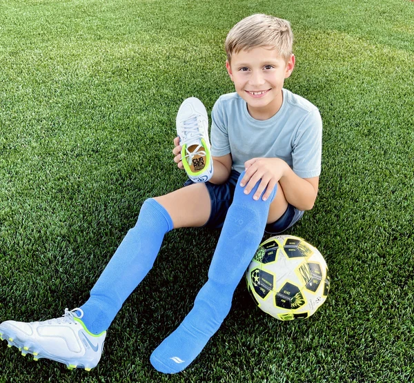 A young soccer player smiling while holding up a cleat